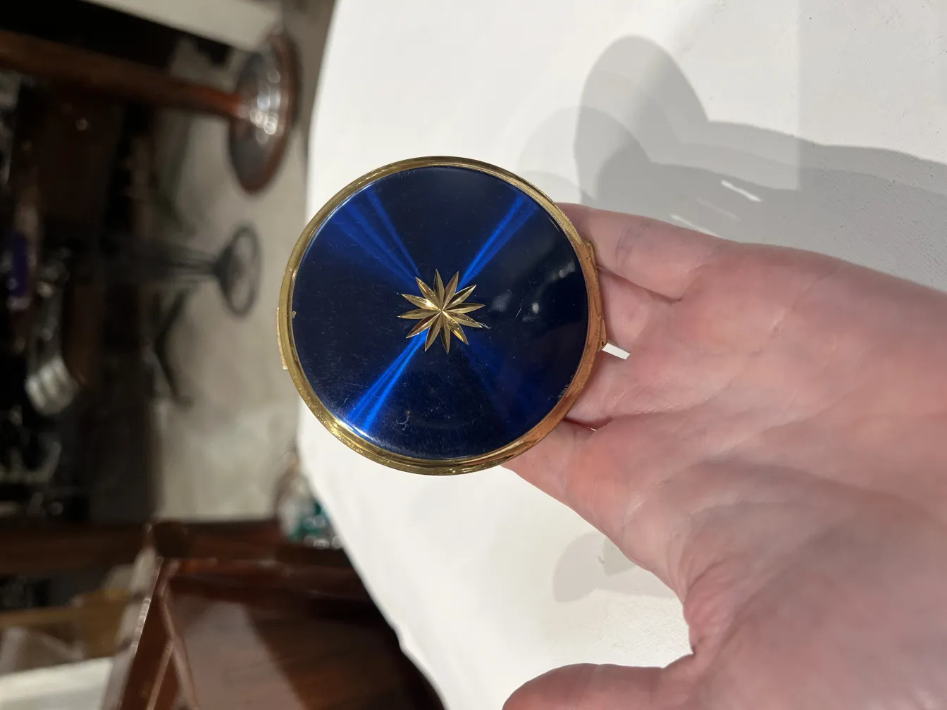 Polvera antigua con un hermoso diseño azul y dorado, sostenida en la mano