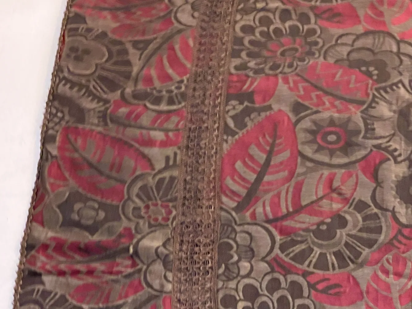 Antike Tischdecke mit roten und grauen Blumen auf einem Tisch.