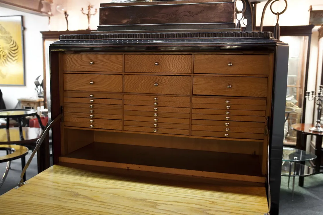 Mueble antiguo para monedas con varios compartimentos y un acabado elegante en un entorno de antigüedades.