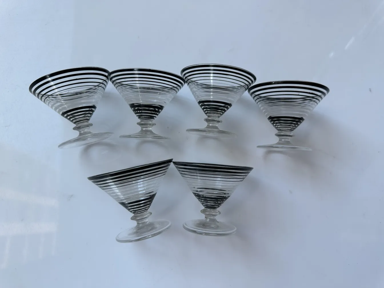 Licoreira antiga e 6 taças com listras decorativas em preto e branco sobre fundo branco.