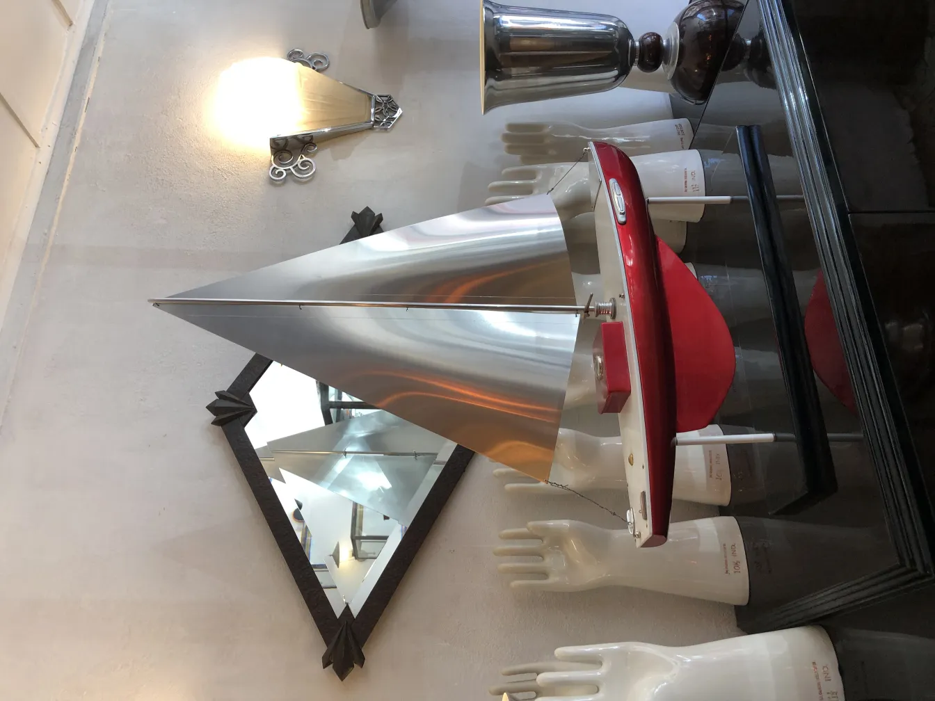 Antiguo barco decorativo del diseñador Marcelo Peña con vela en forma de cono y base roja en un ambiente artístico.