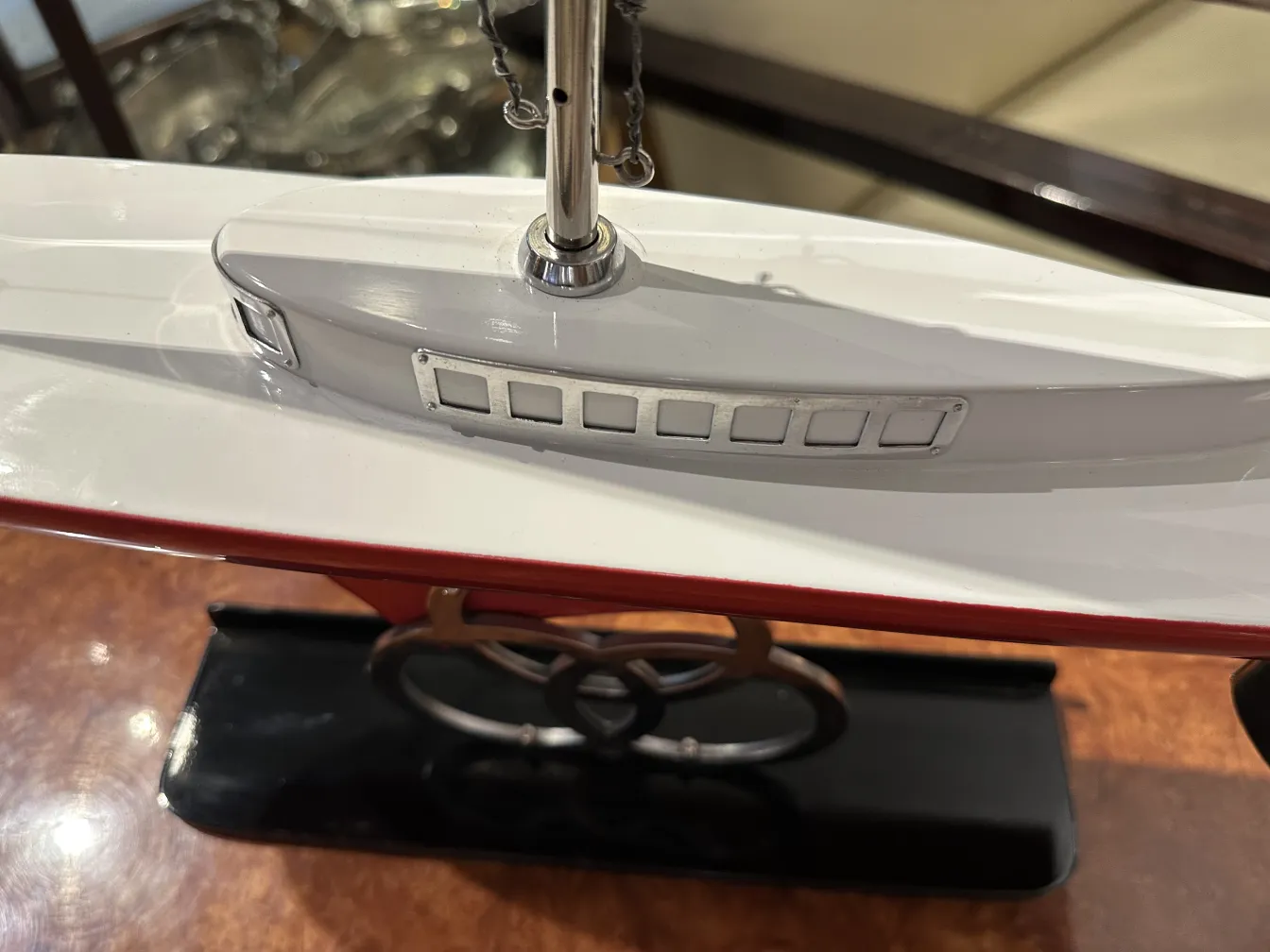 Modelo em escala de um barco antigo do designer Marcelo Peña, com detalhes visíveis como janelas e um acabamento brilhante em vermelho e branco.
