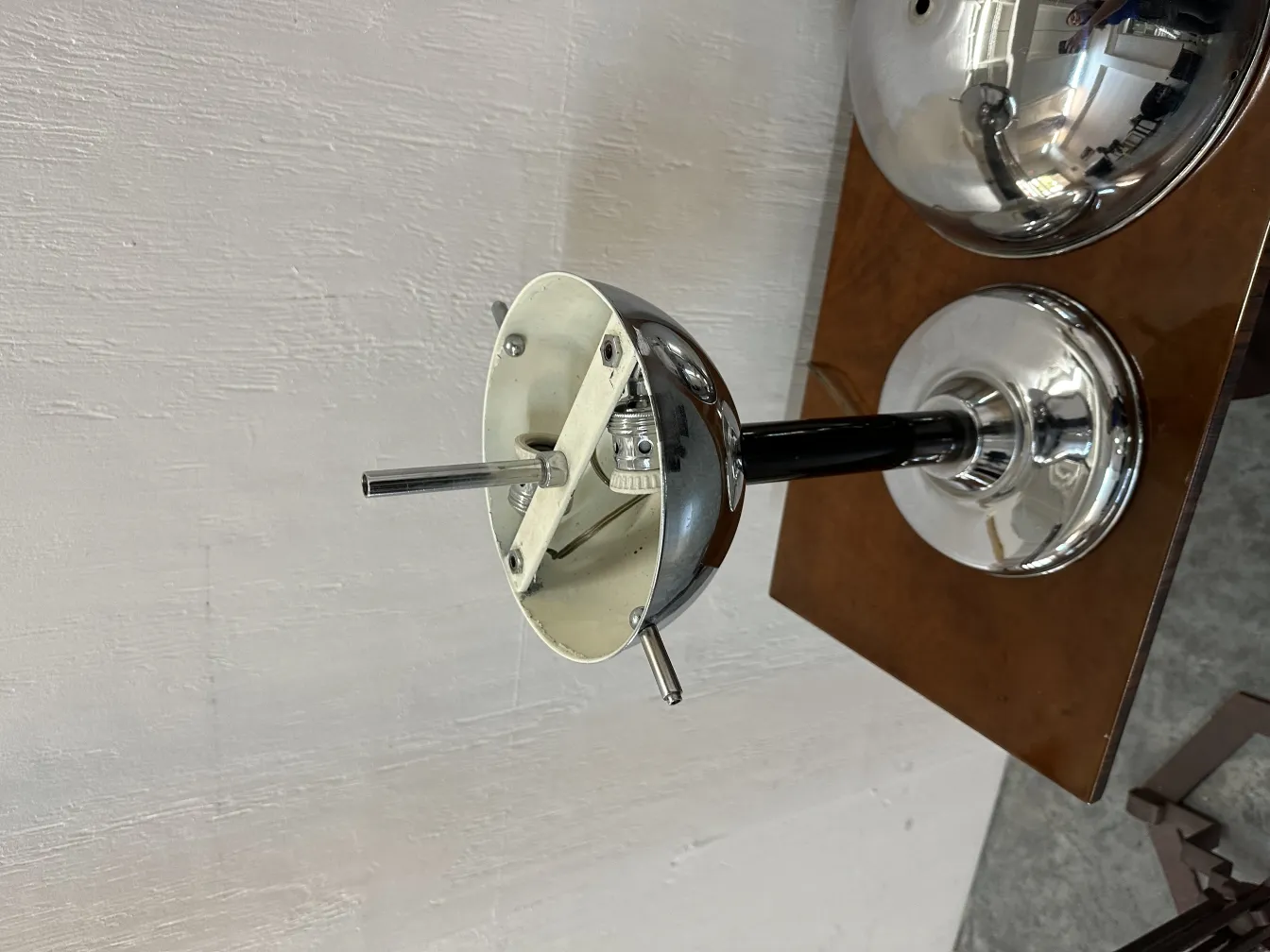 Antica lampada da tavolo con base metallica rotonda lucida, stile classico, in un ambiente neutro.