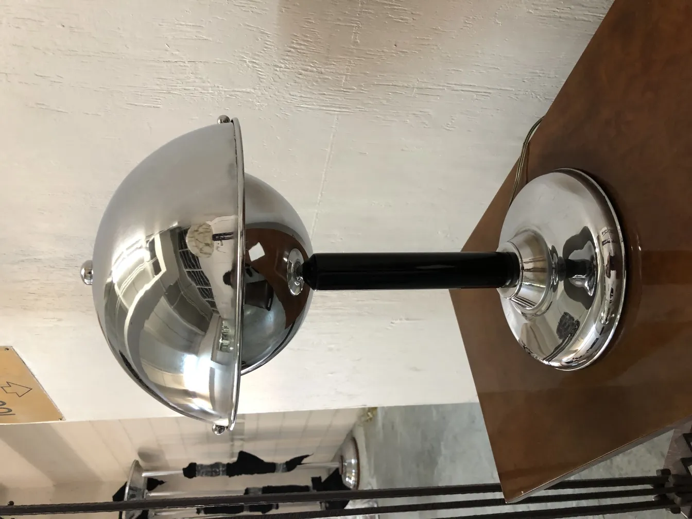 Luminária de mesa antiga com cúpula cônica e base polida, sobre uma mesa de madeira.