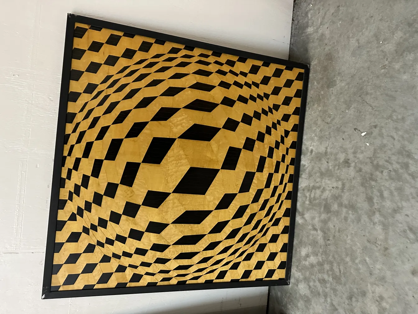 Antiga marchetaria com padrões geométricos em tons de dourado e preto, com uma moldura elegante.