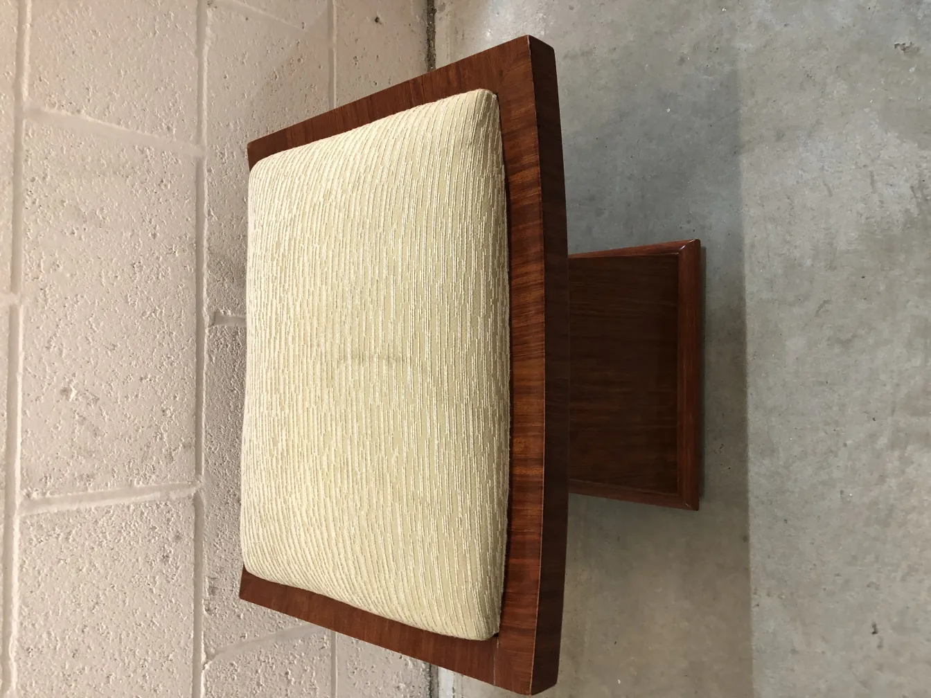 Antique stool with beige cushion in a neutral setting.