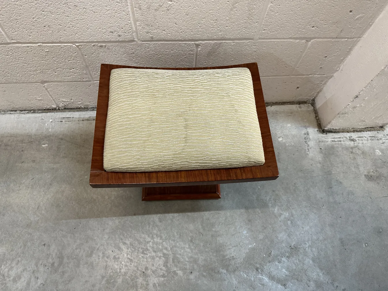 Tabouret ancien avec coussin crème et design classique.