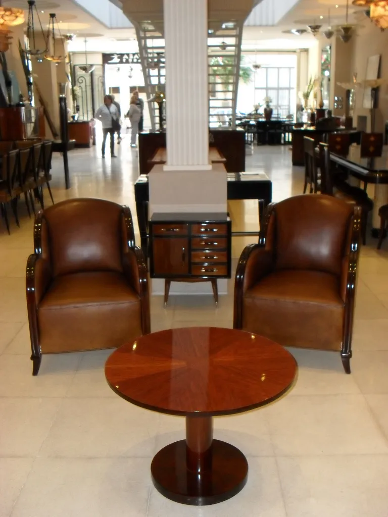 Tavolino antico con finitura lucida, forma rotonda, in un ambiente elegante con poltrone in pelle.