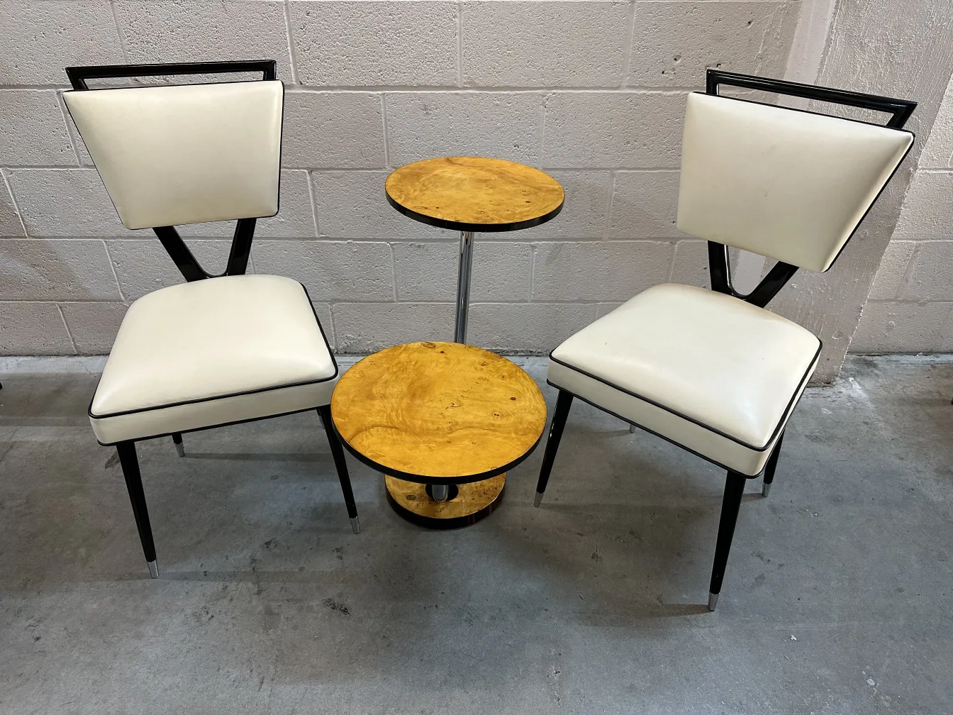 petite table ancienne entre des chaises blanches sur le sol gris