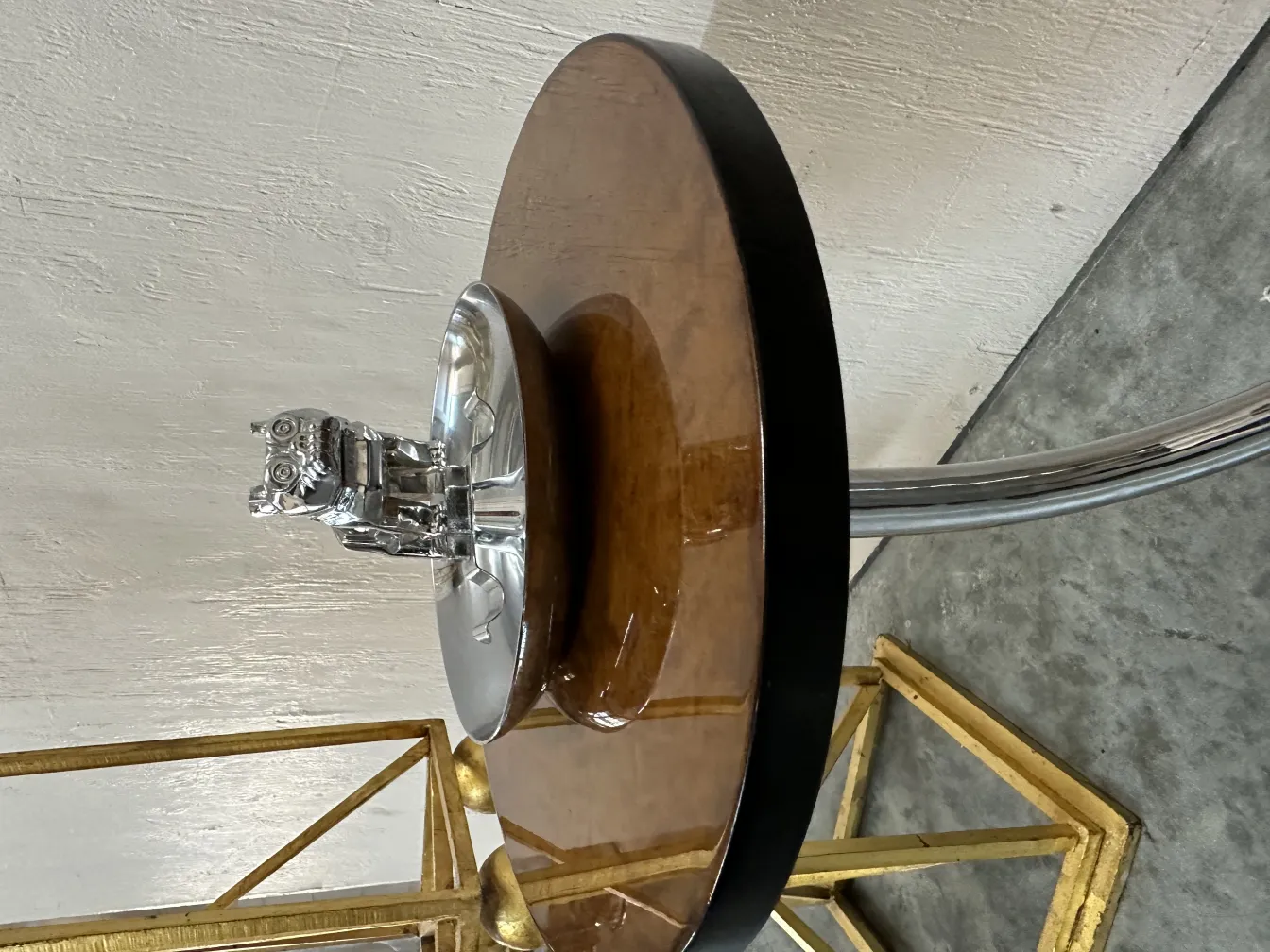 Tavolino antico con design circolare e oggetto decorativo sopra, su un pavimento testurizzato.