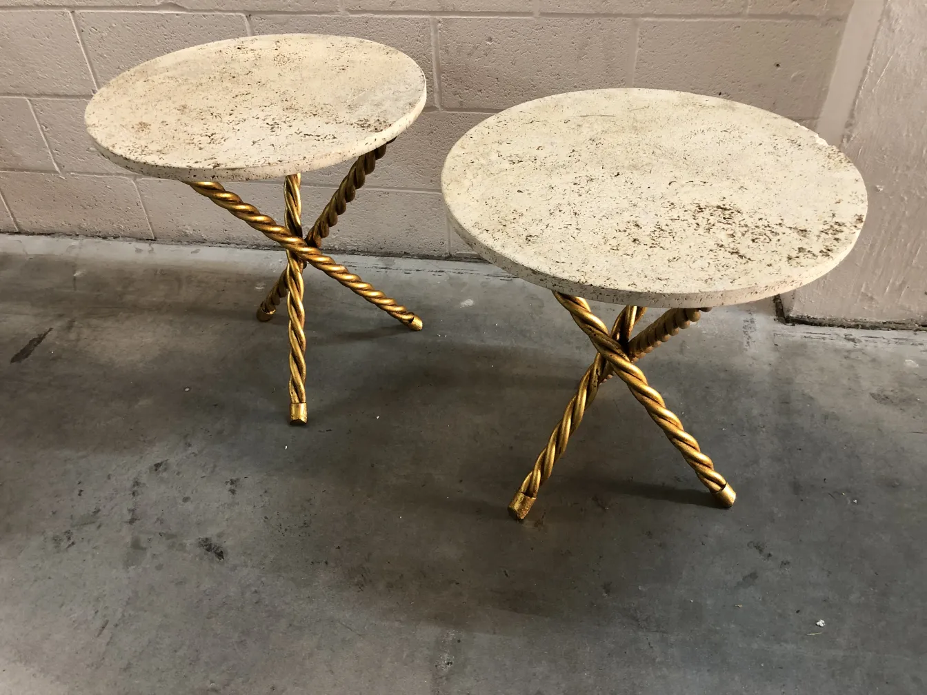 Conjunto de dos mesitas antiguas con patas trenzadas doradas y superficie redonda.