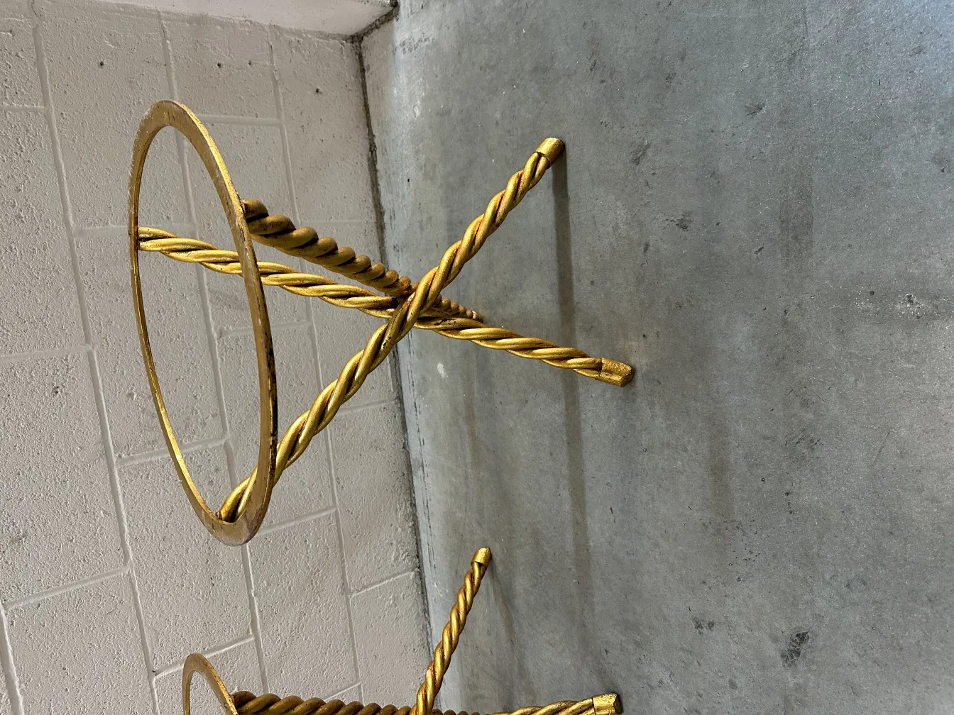 Two antique small tables with gold base and intricate design, set in a concrete environment.
