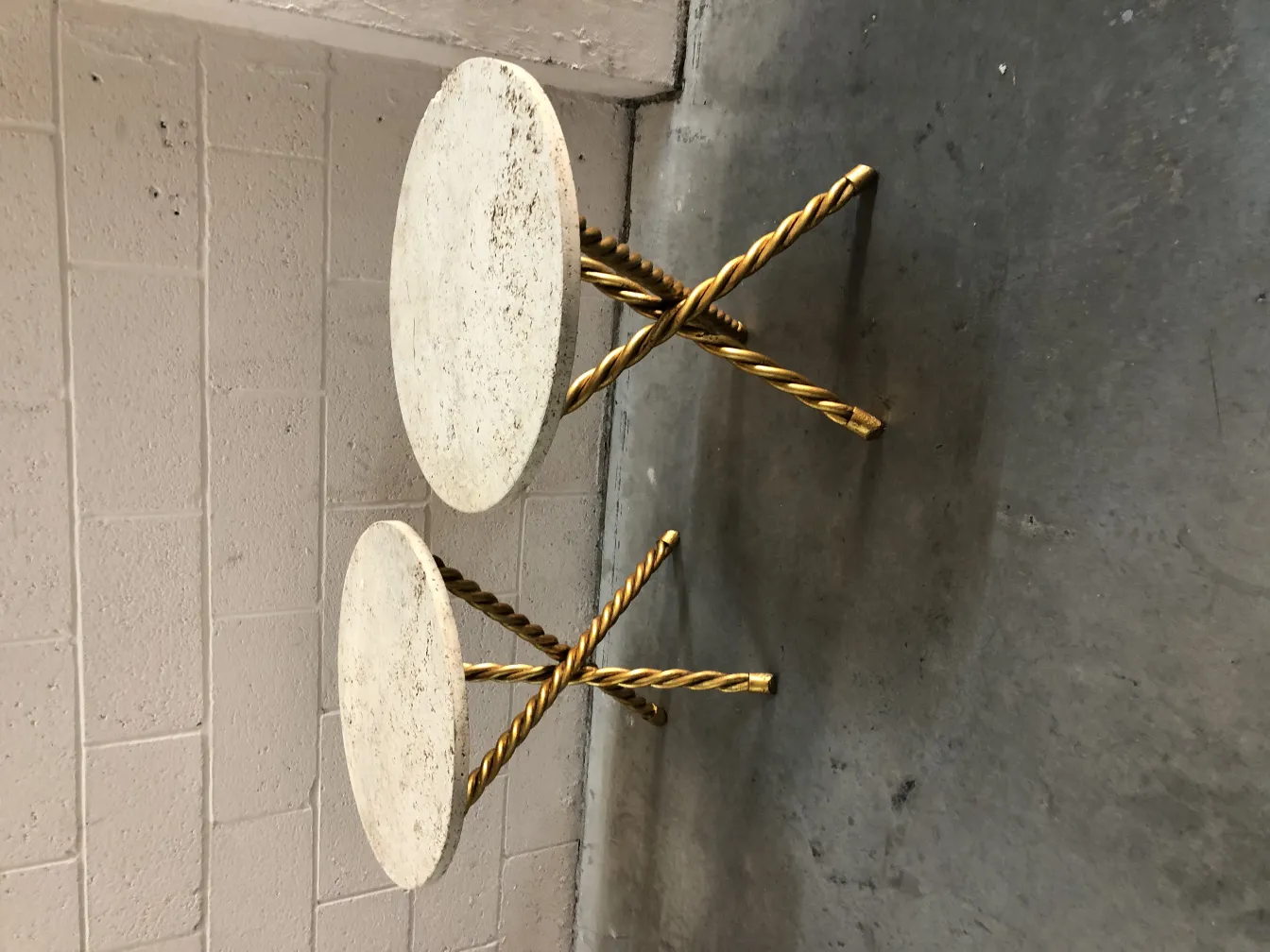 Deux petites tables antiques avec dessus rond et pieds dorés dans un cadre neutre.