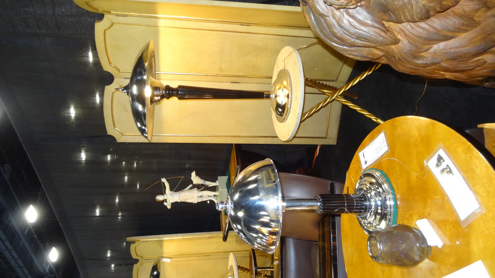 2 tavolini antichi in un ambiente decorativo, con una lampada e una figura sullo sfondo.