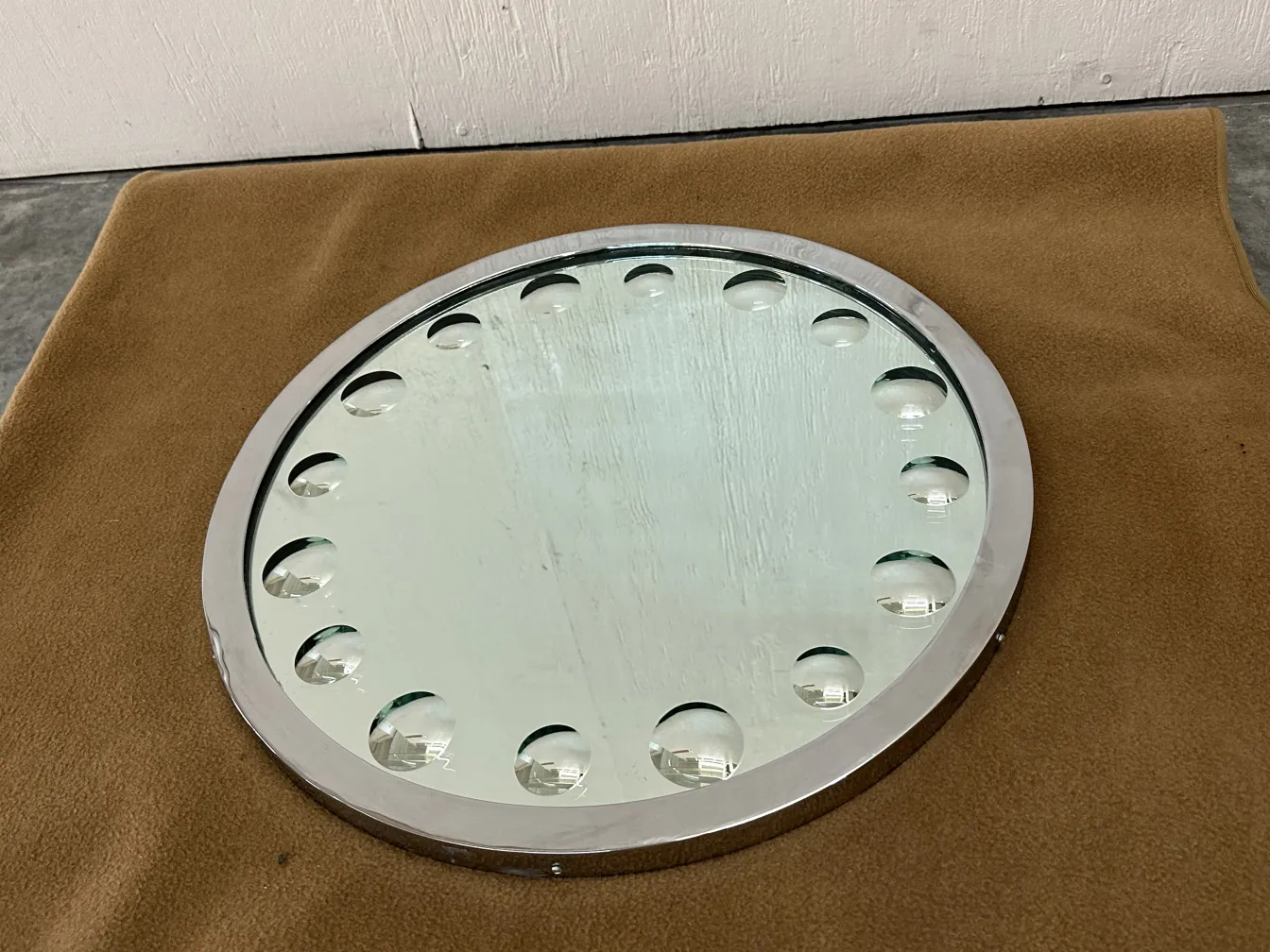 Miroir rond antique avec détails sur les bords, posé sur une surface douce.