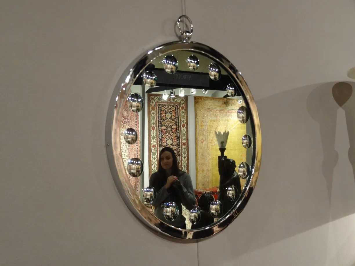 Miroirs anciens décoratifs avec des lumières rondes autour du bord, sur un mur blanc.