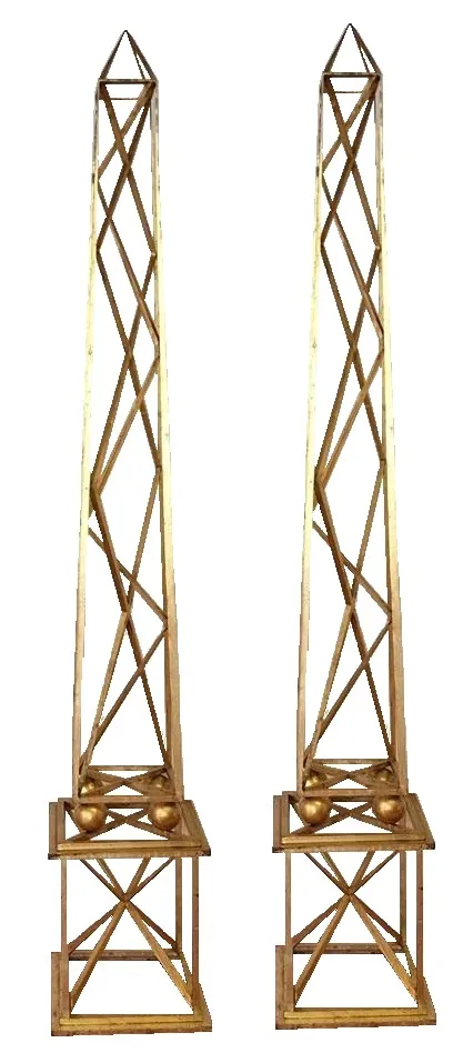 Descripción de dos obeliscos antiguos decorativos, altos y elegantes. Destcan en el ambiente decorativo.