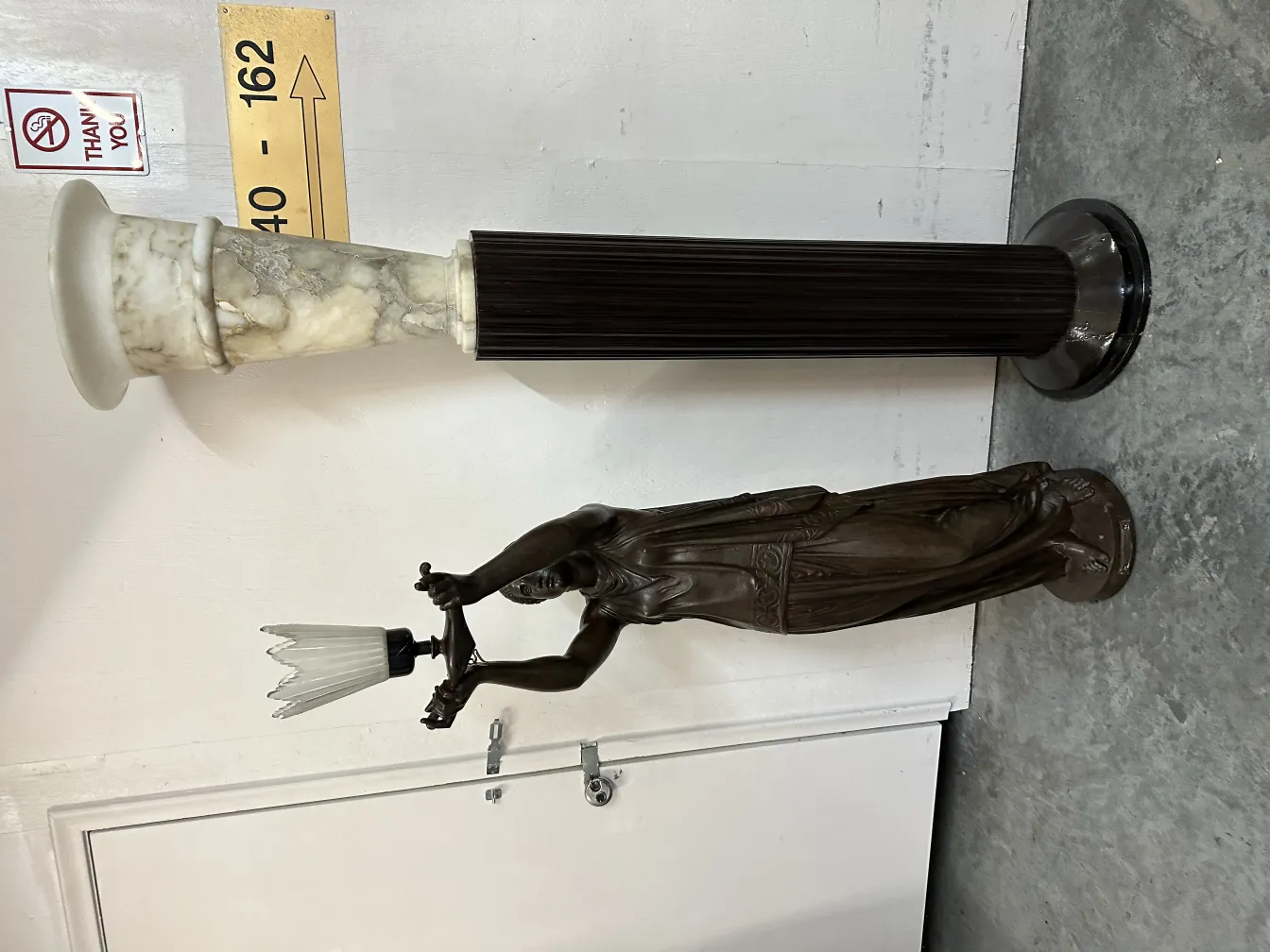 escultura antigua con figura femenina sosteniendo lámpara de cristal, fondo claro.