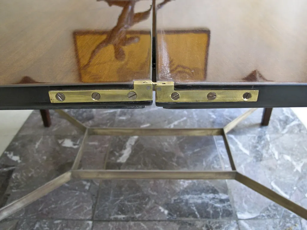 Mesa de jantar antiga com detalhes decorativos e ferragens visíveis, situada em um ambiente clássico.