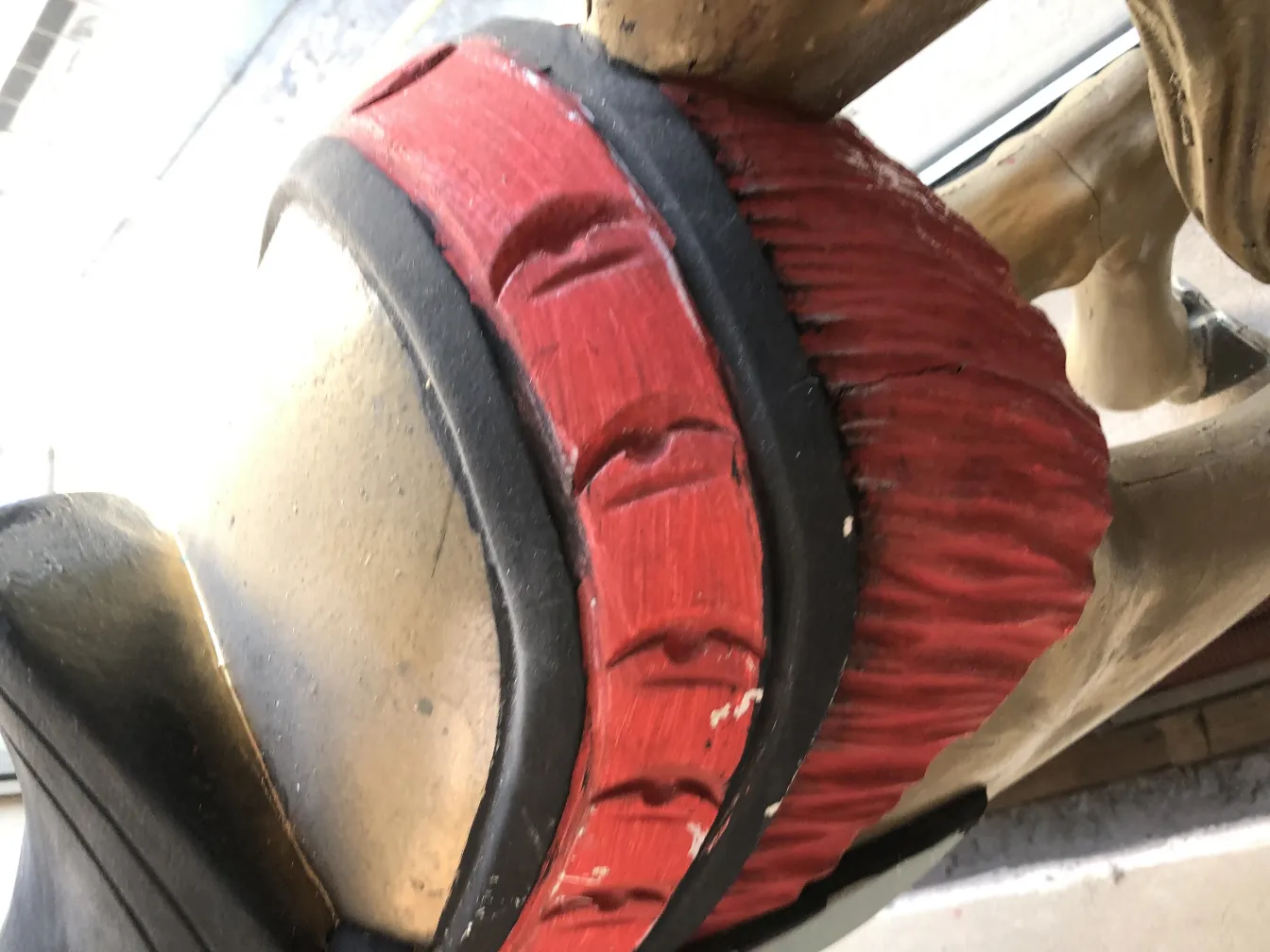 Estátua antiga de unicórnio com detalhes em vermelho e preto, fundo neutro.