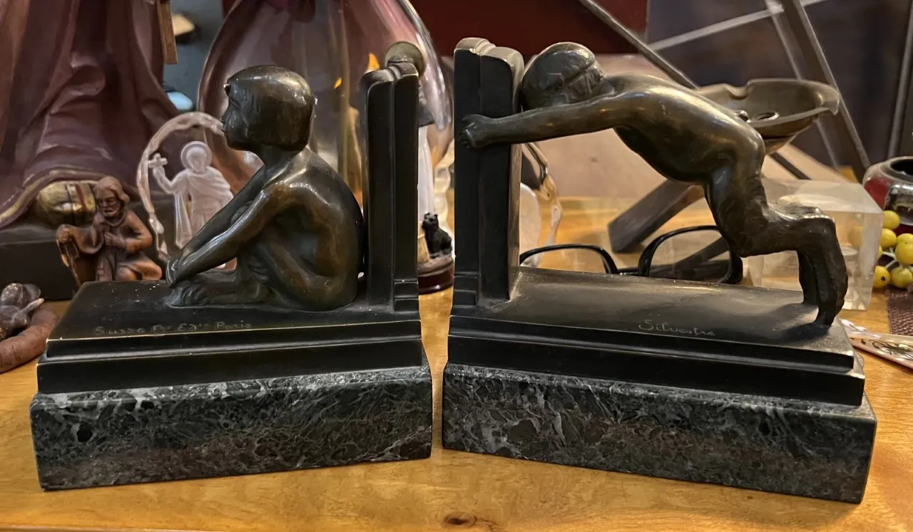 Serre-livres antiques avec sculptures d'enfants en bronze, entourés d'objets décoratifs.