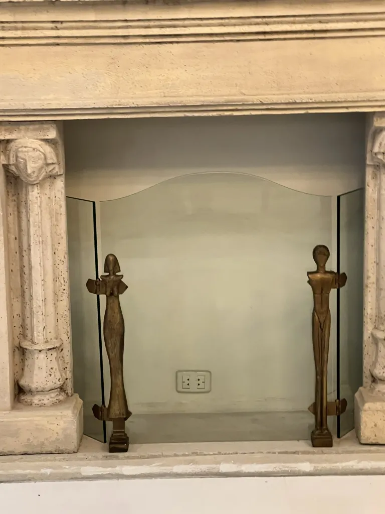 fronte del camino antico con figure dell'artista alberto giacometti, inserito in un ambiente interno. figure stilizzate ai lati.