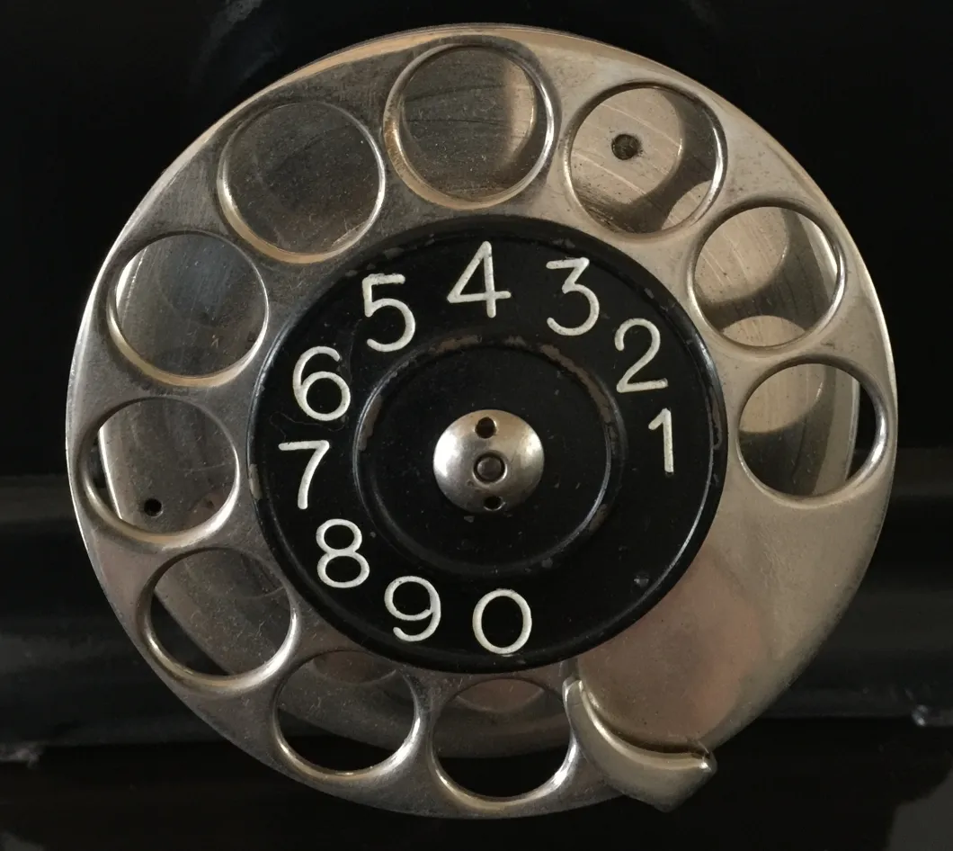 Vue de dessus d'un téléphone ancien à cadran rotatif, avec des détails noirs et argentés.