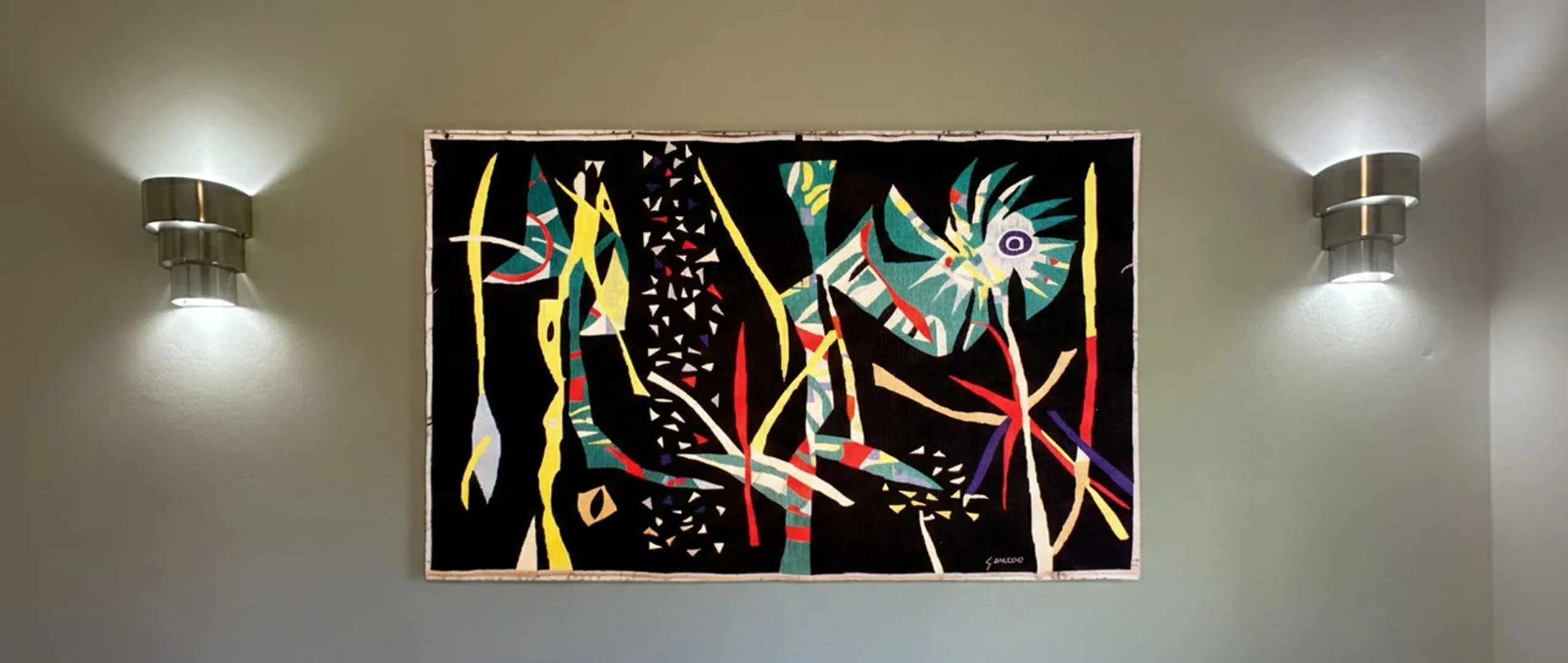 Par de apliques antiguos en la pared, con una pintura colorida detrás.