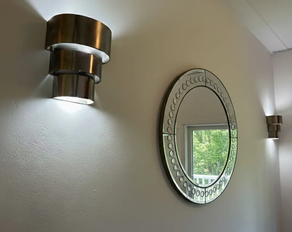 paire d'appliques anciennes avec lumières sur un mur blanc, avec un miroir rond à côté