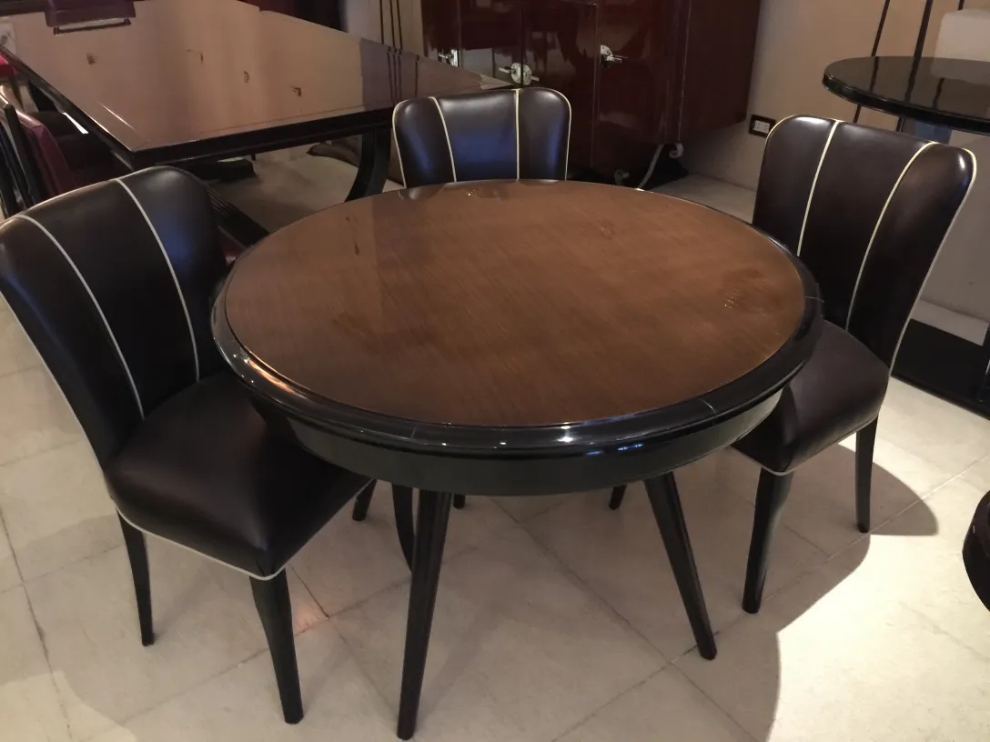 Round antique dining table for four people with black chairs in an elegant setting.