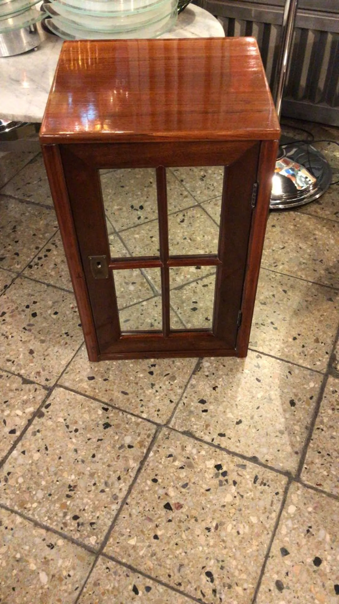 mesa de luz antigua con puerta de cristal, ubicada en un piso de cerámica