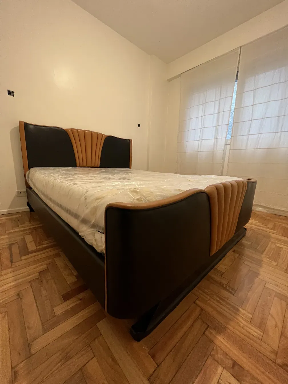 Antikes Art Deco Bett mit Kopfteil in dunklen und hellen Tönen, warmes Ambiente.
