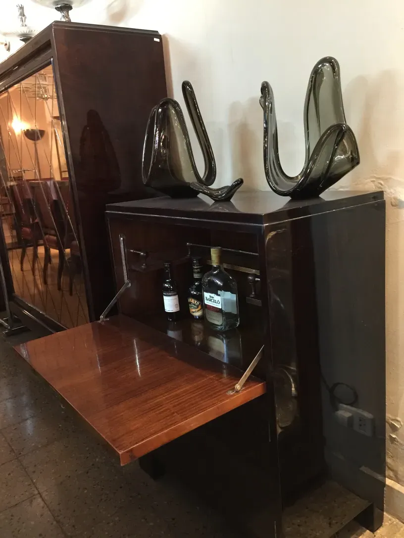 mueble bar antiguo con fondo de vidrio y botellas, accesorios decorativos en la parte superior.