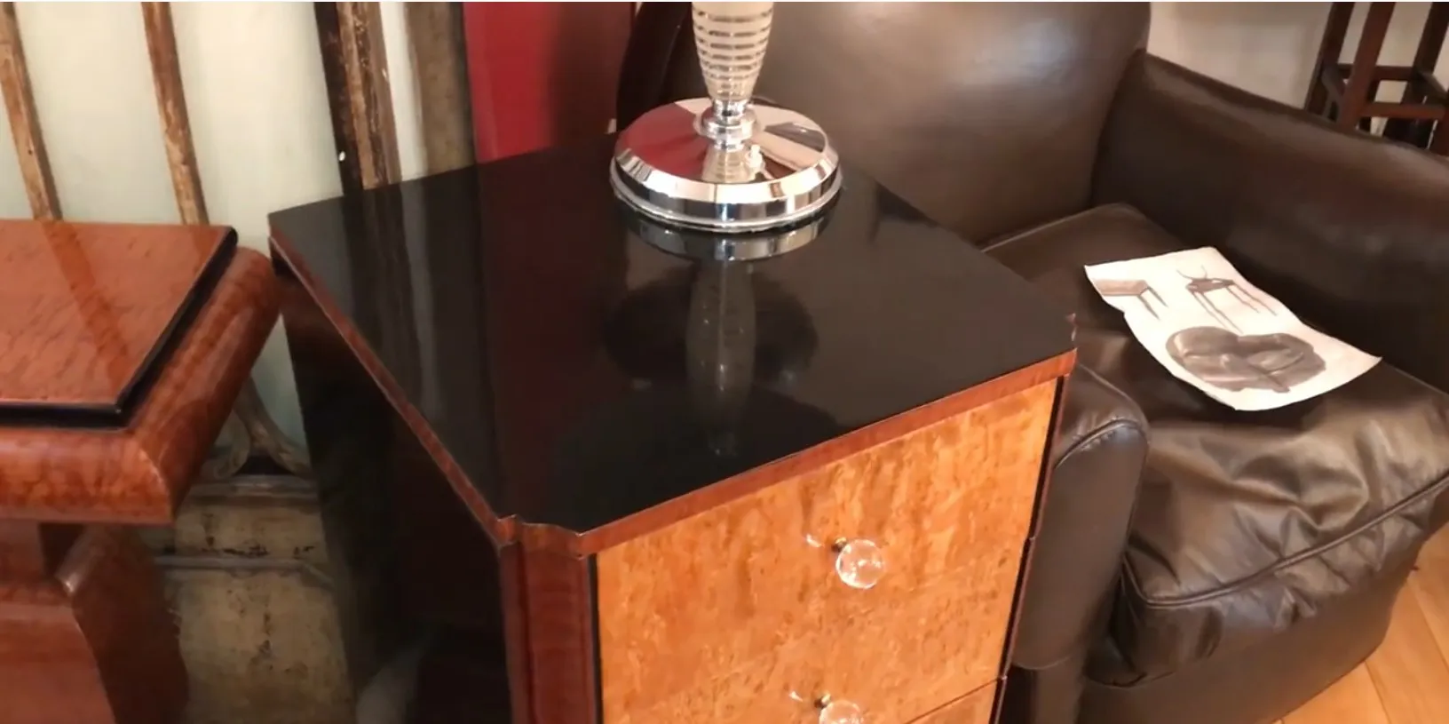 Cassettiera antica in legno con finitura lucida e maniglie in cristallo, accanto a un divano marrone.