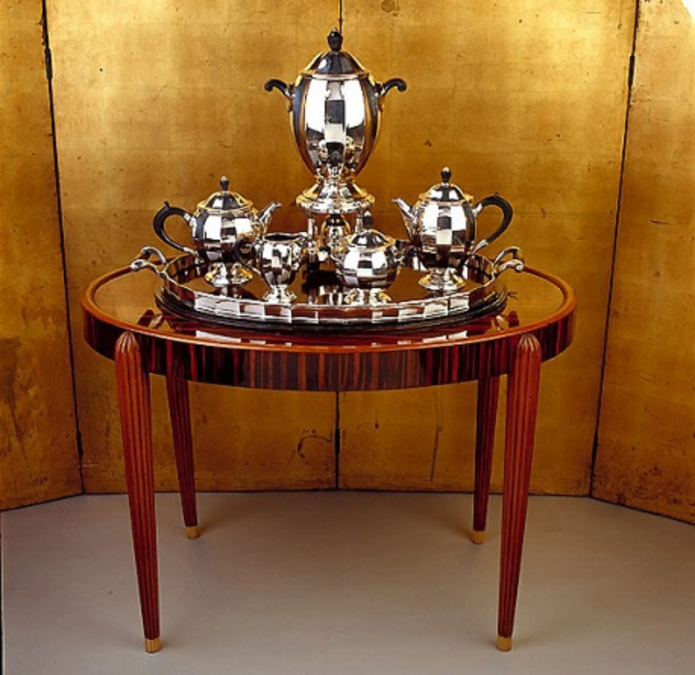 Antiker kleiner Tisch mit elegantem Teeservice darauf, goldener Hintergrund.