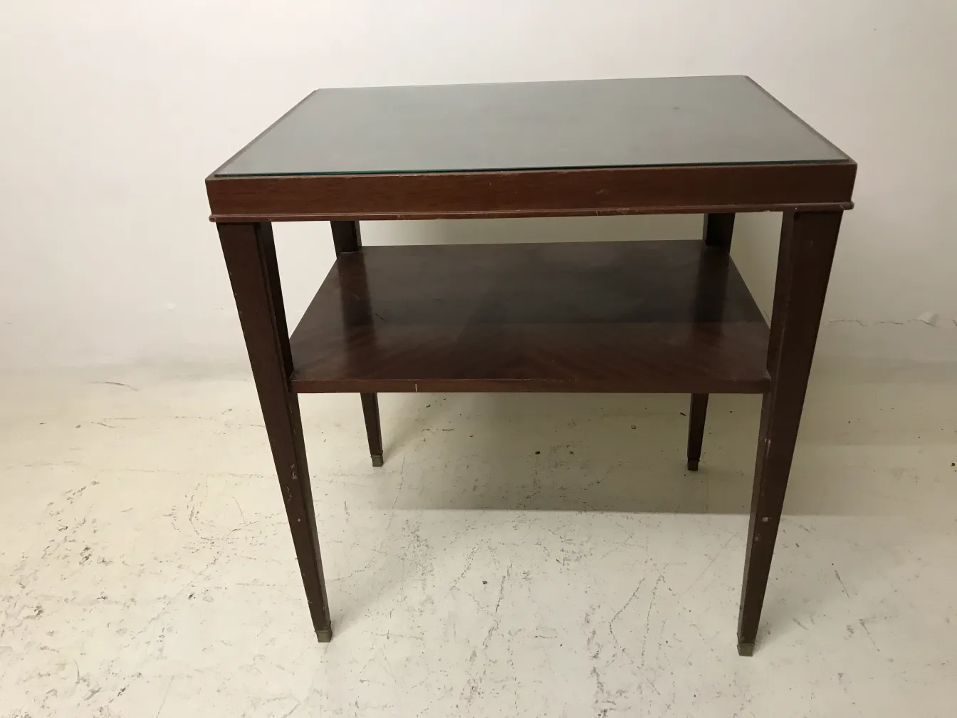 Mesa antigua Art Deco con una superficie de vidrio, estante inferior y patas elegantes en ambiente minimalista.