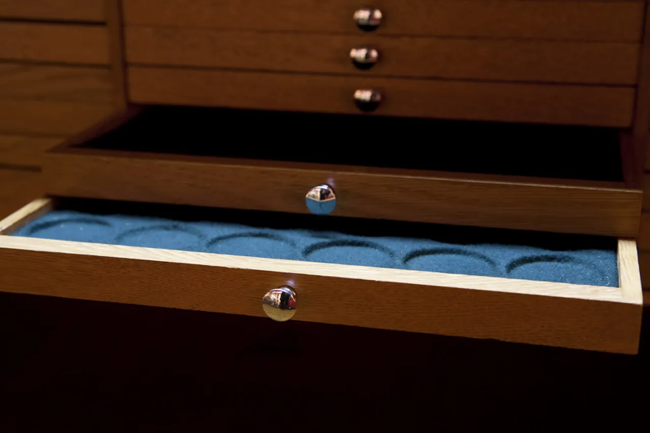 Vista de um armário antigo para moedas com compartimentos internos em um ambiente escuro.