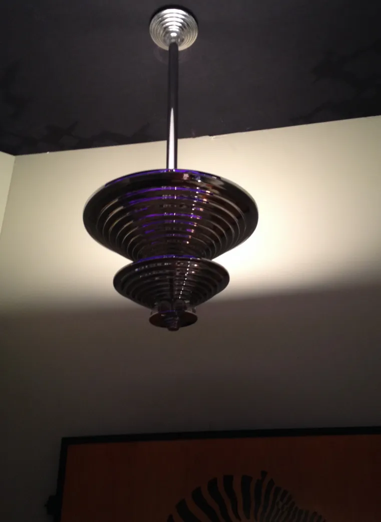 Lampada a sospensione antica con design circolare e stile art deco, illumina un ambiente neutro.