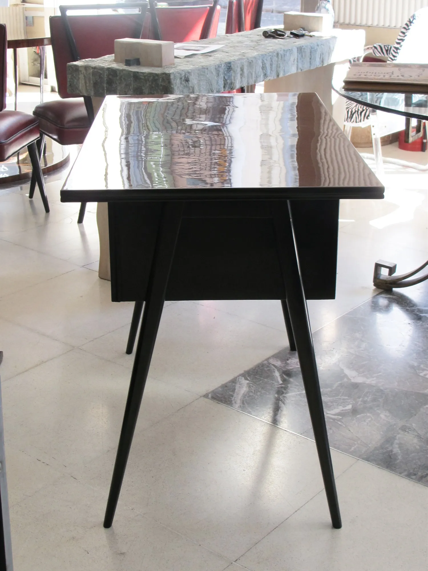 Antique desk with minimalist design, thin legs and shiny surface, surrounded by furniture