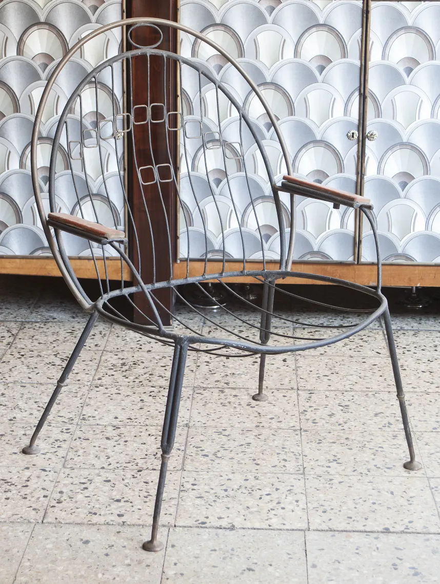 Sillón de jardín antiguo con brazos, estilo sencillo, rodeado de un ambiente acogedor.