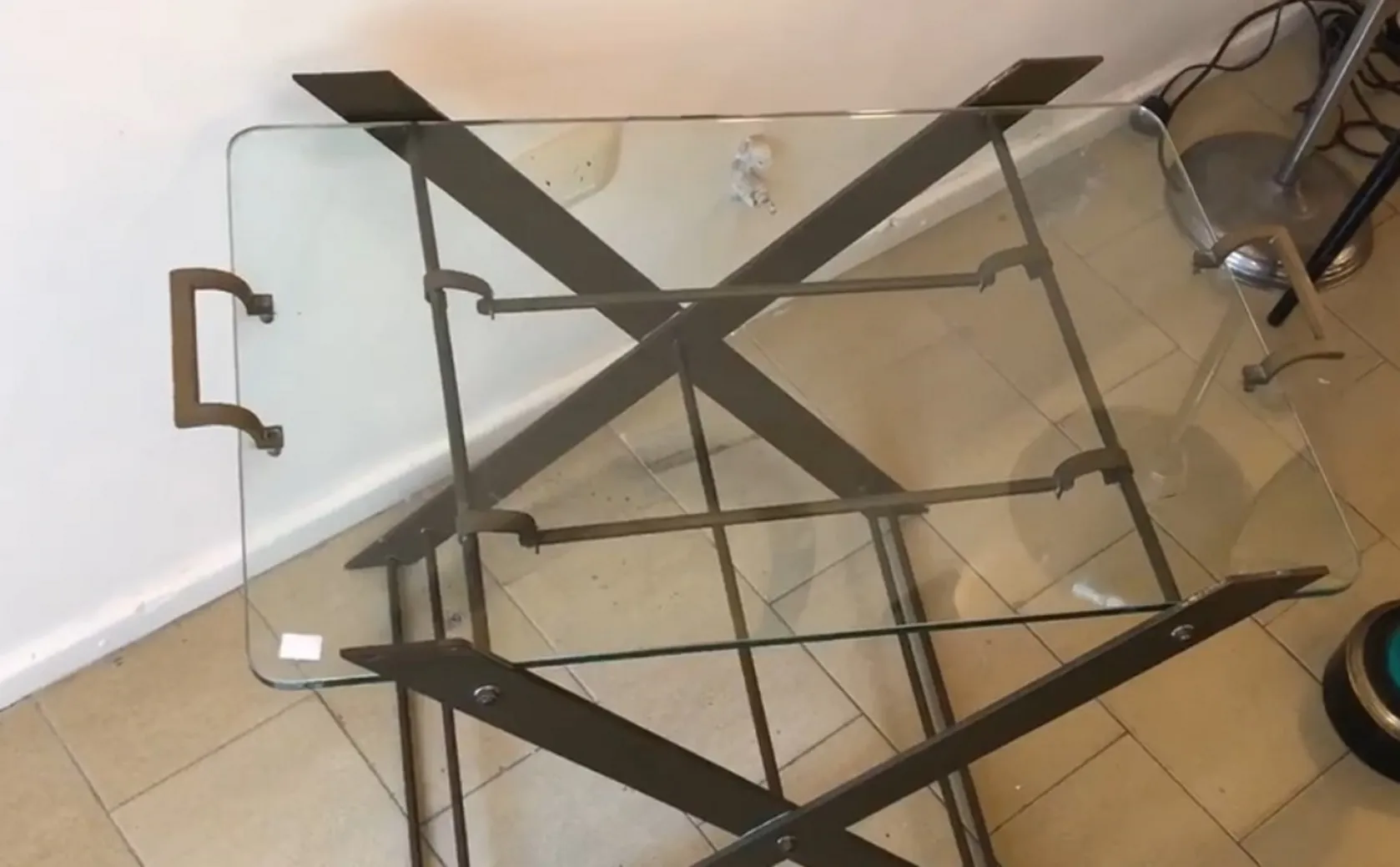 mesita antigüedad con superficie de cristal transparente y base metálica cruzada en un ambiente moderno