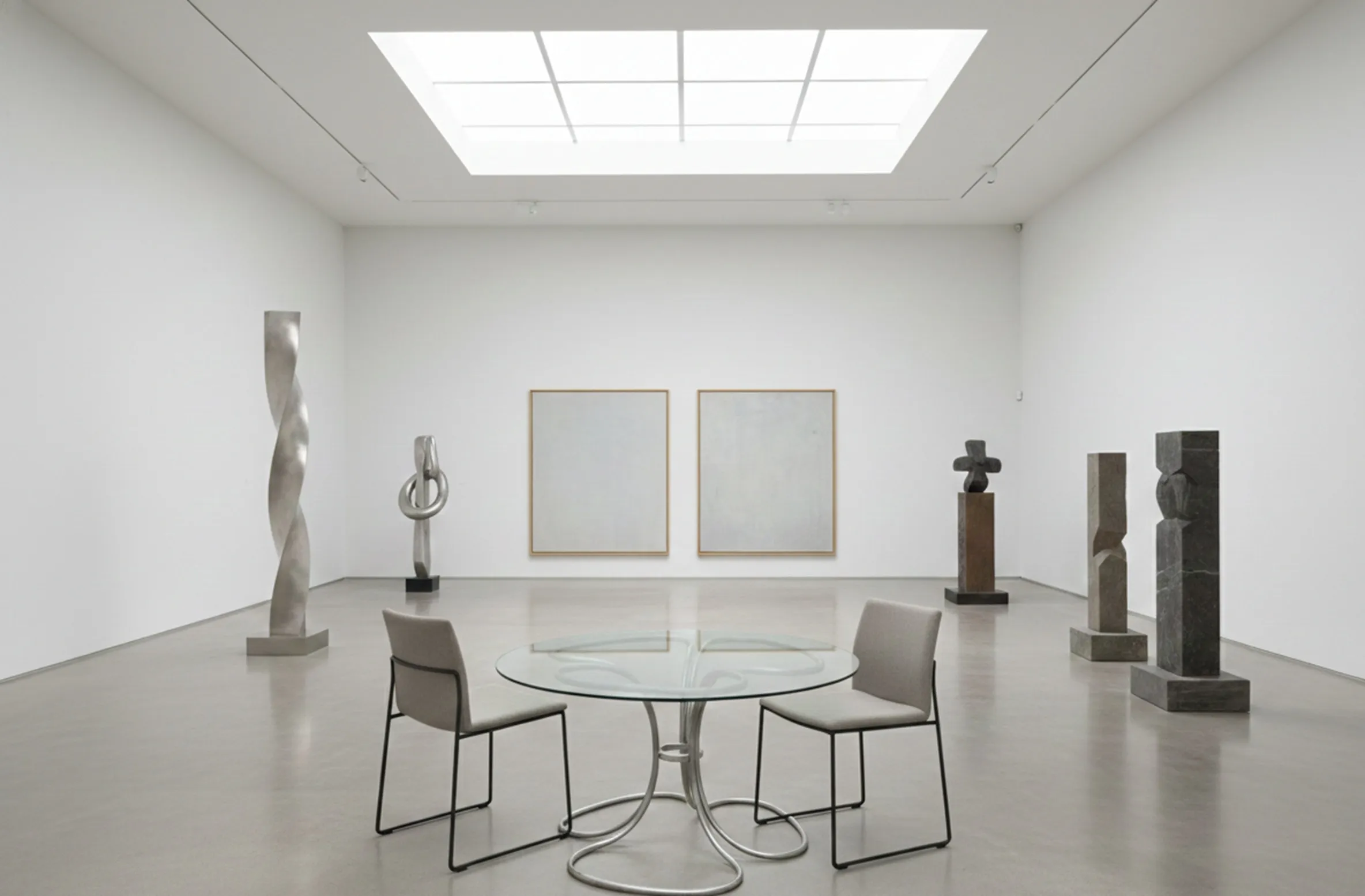 Mesa de comedor de antigüedad para seis personas, en un entorno minimalista con esculturas de arte moderno.