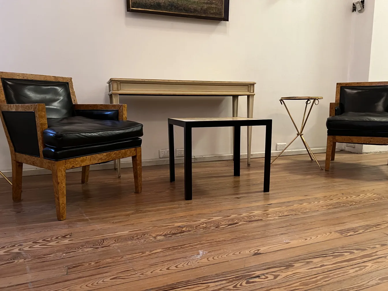 Two armchairs in a stylish setting, with a table and art on the wall.