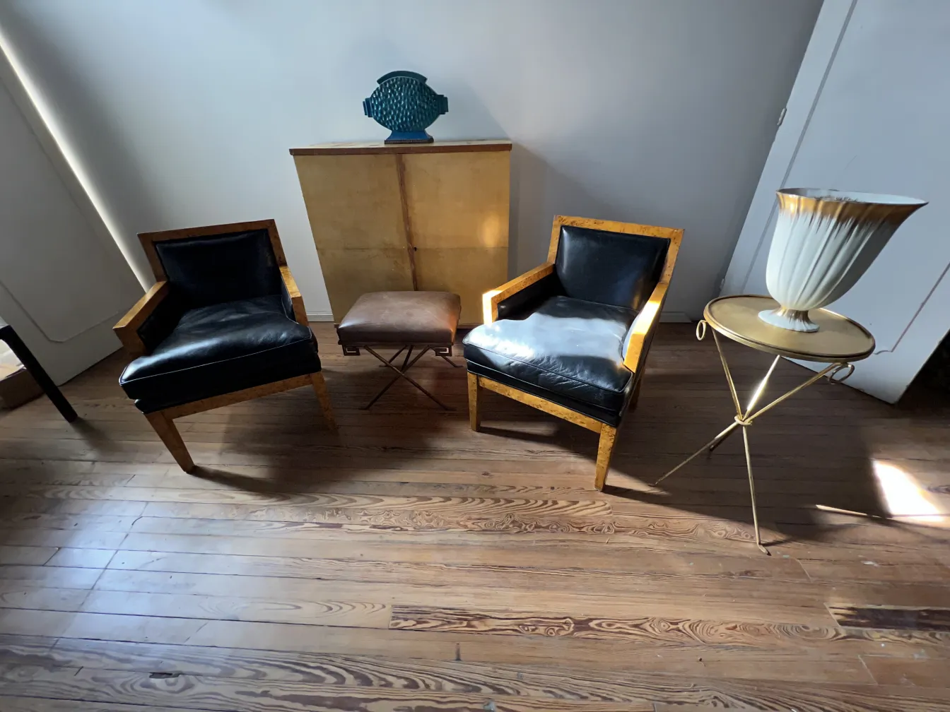 Deux fauteuils anciens avec des sièges noirs, à côté d'une petite table.