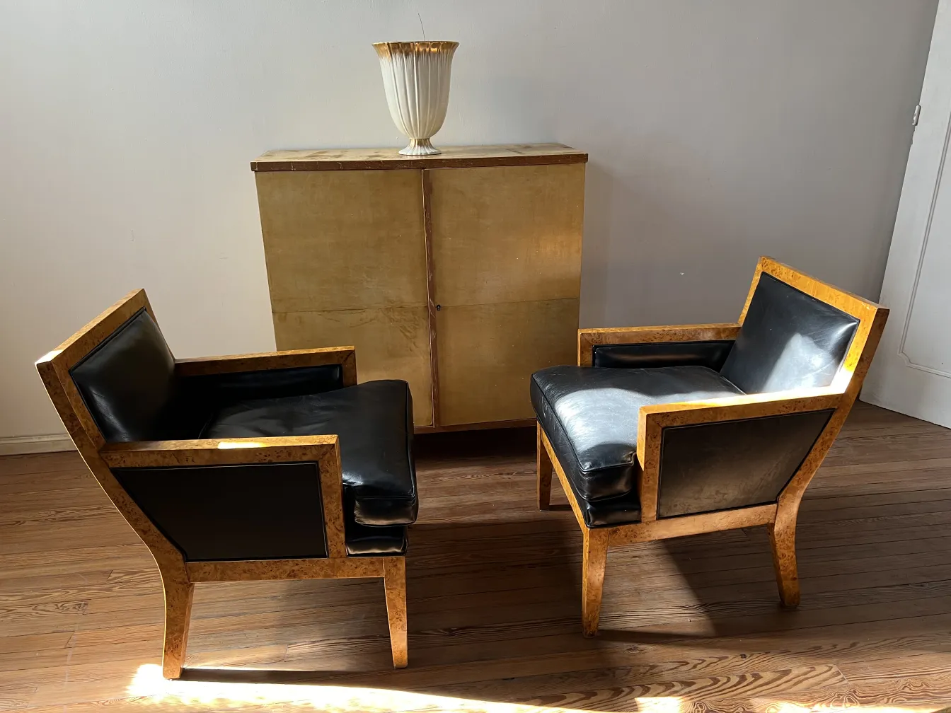 dos sillones antiguos con estructura de madera clara y tapizado negro, en un ambiente minimalista