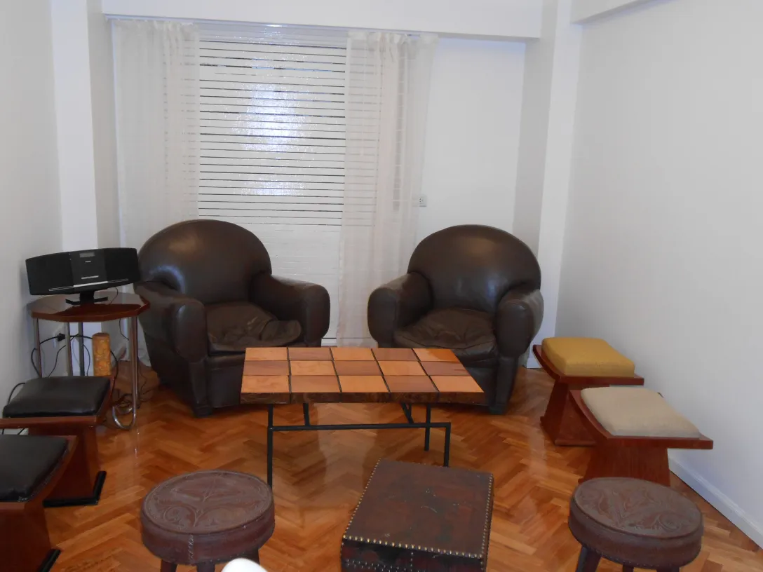 dos sillones antiguos en una sala, uno de ellos en primer plano, iluminados por luz natural, en un ambiente relajante.