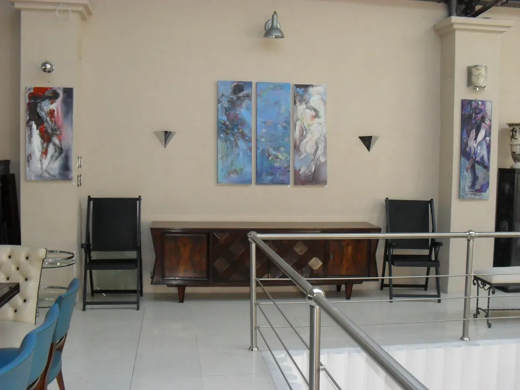 दो प्राचीन आर्मचेयर की मरम्मत एक सजावटी सेटिंग में की जानी है, जिसमें आधुनिक कला है।