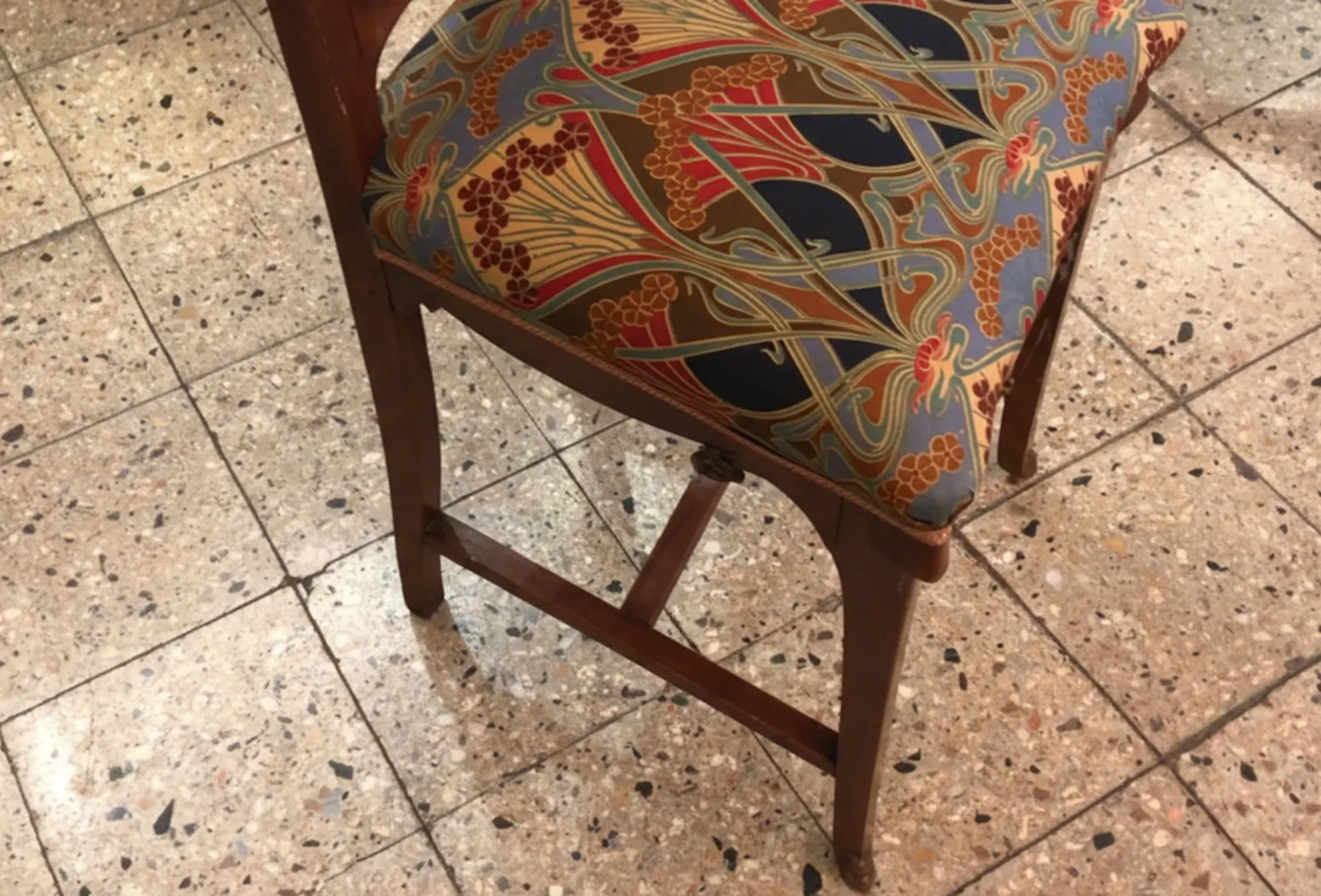 Silla antigua con respaldo y estampado colorido, en un ambiente de antigüedades.