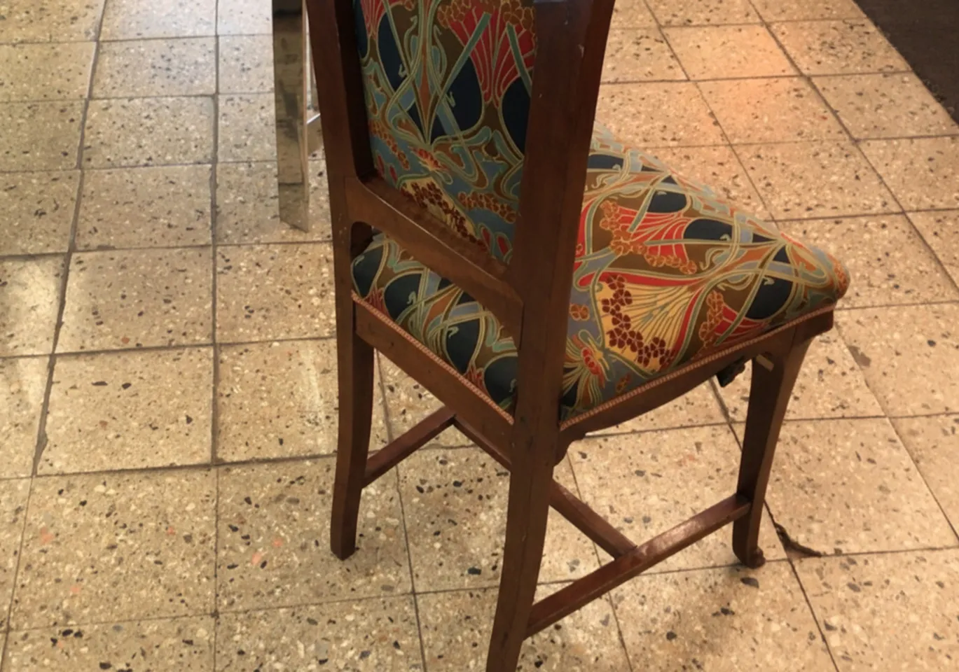 Silla antigua de estilo Art Nouveau con coloridos diseños en el respaldo, en un entorno acogedor.