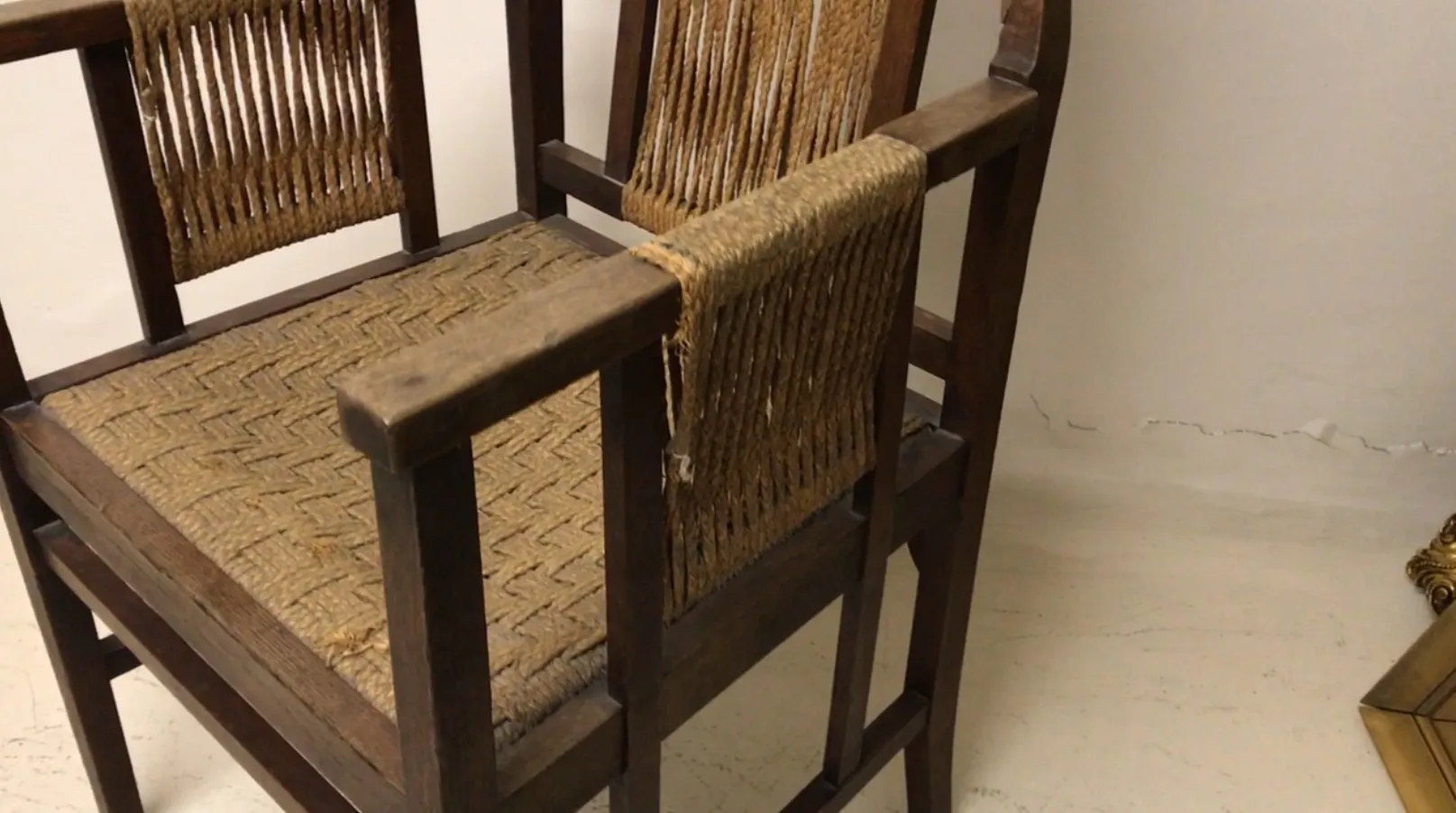 Sillón de escritorio antiguo con respaldo trenzado y asiento de caña, en un ambiente neutro.